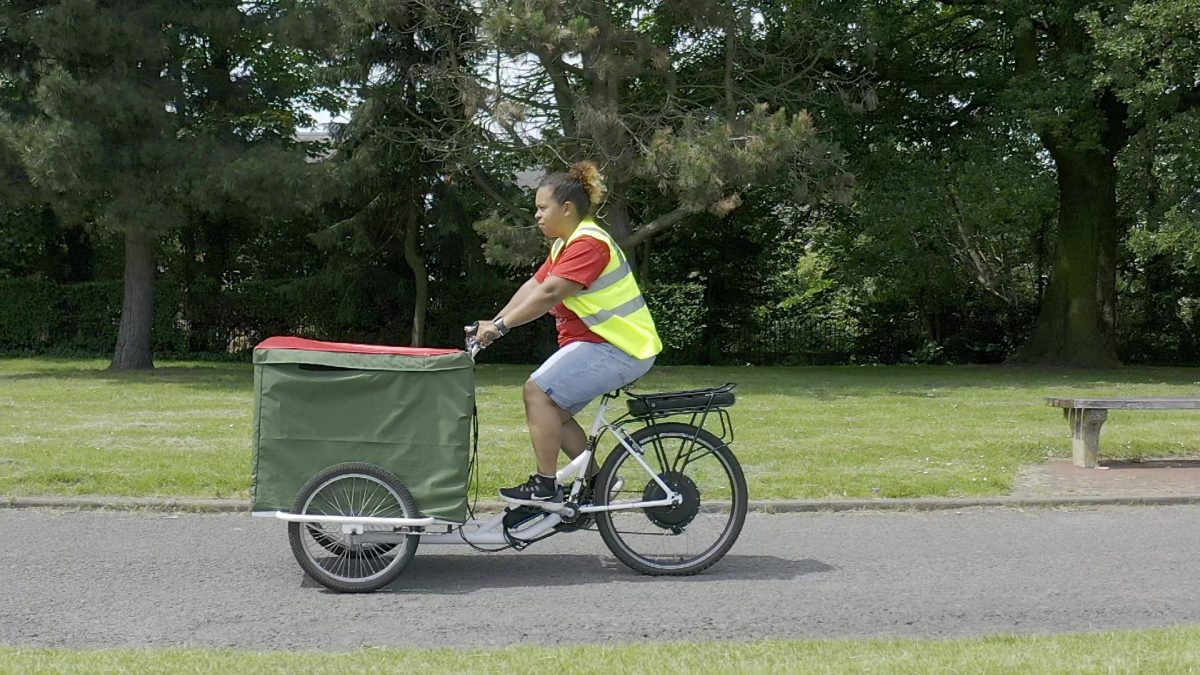 a women wearing a high vis jacket is cycling in a park. 