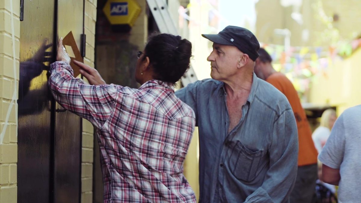 a women we see from the back and a man are looking at a wall on the left, they are fixing the wall