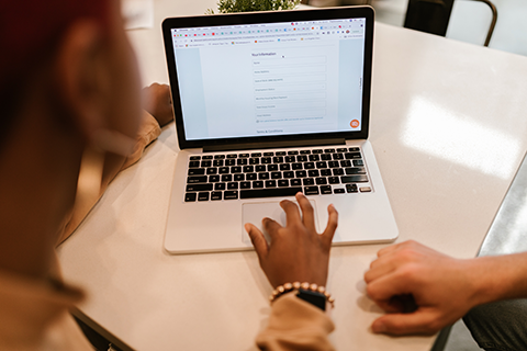 A laptop on a desk. We can see two people working on it from the back