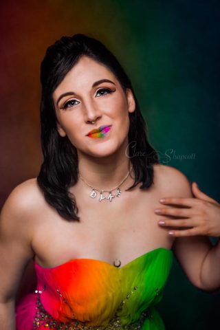 a women is looking at the camera wearing a dress with rainbow colours and rainbow lipstick