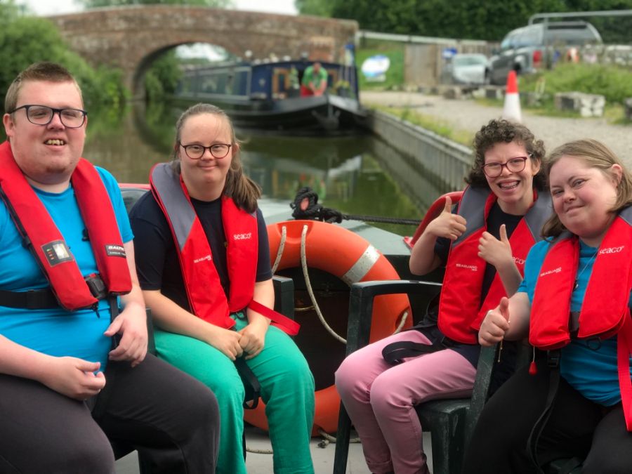 4 young people are sitting on a boat, wearing life vests and smiling at the camera