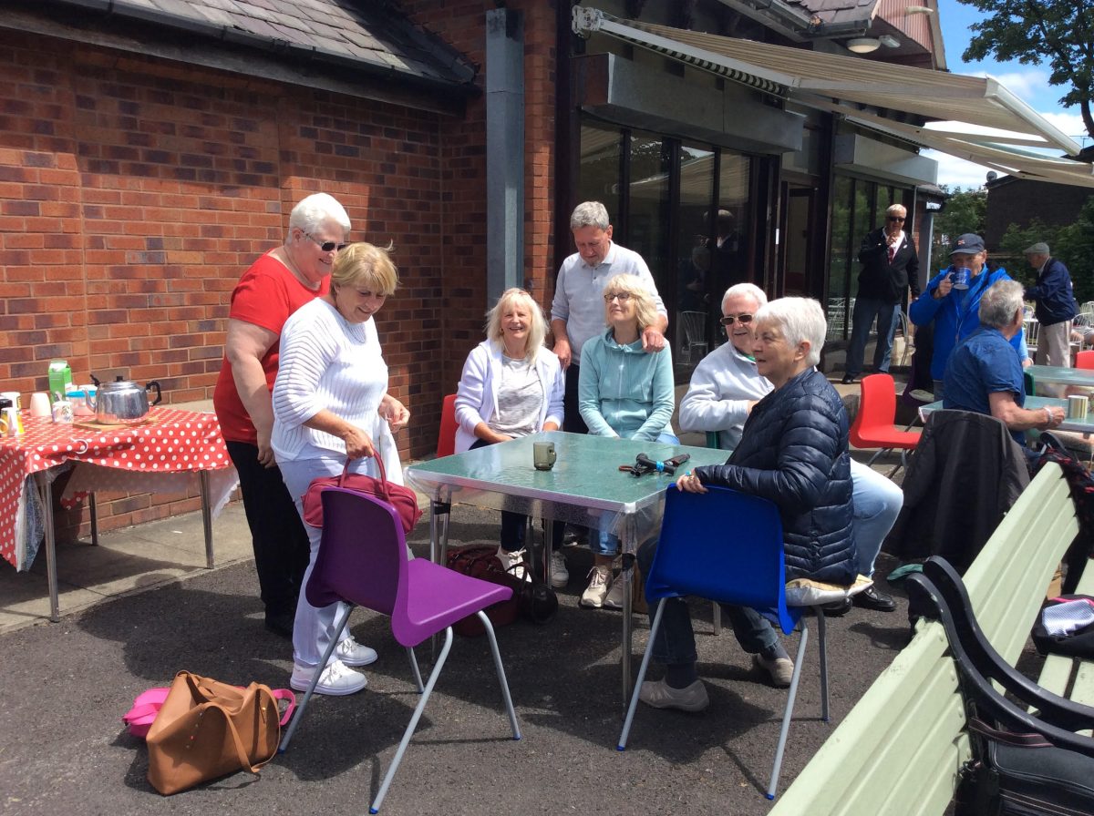 A group of elderly people is gathered around a table, chilling in the sun. 